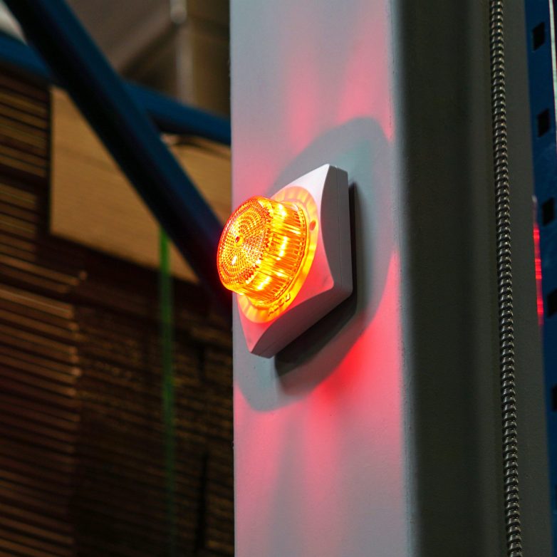 An image of an Algo 8138 visual alerter device securely mounted on a wall. The alerter is a square unit with a bright strobe light that can change colours and patters.