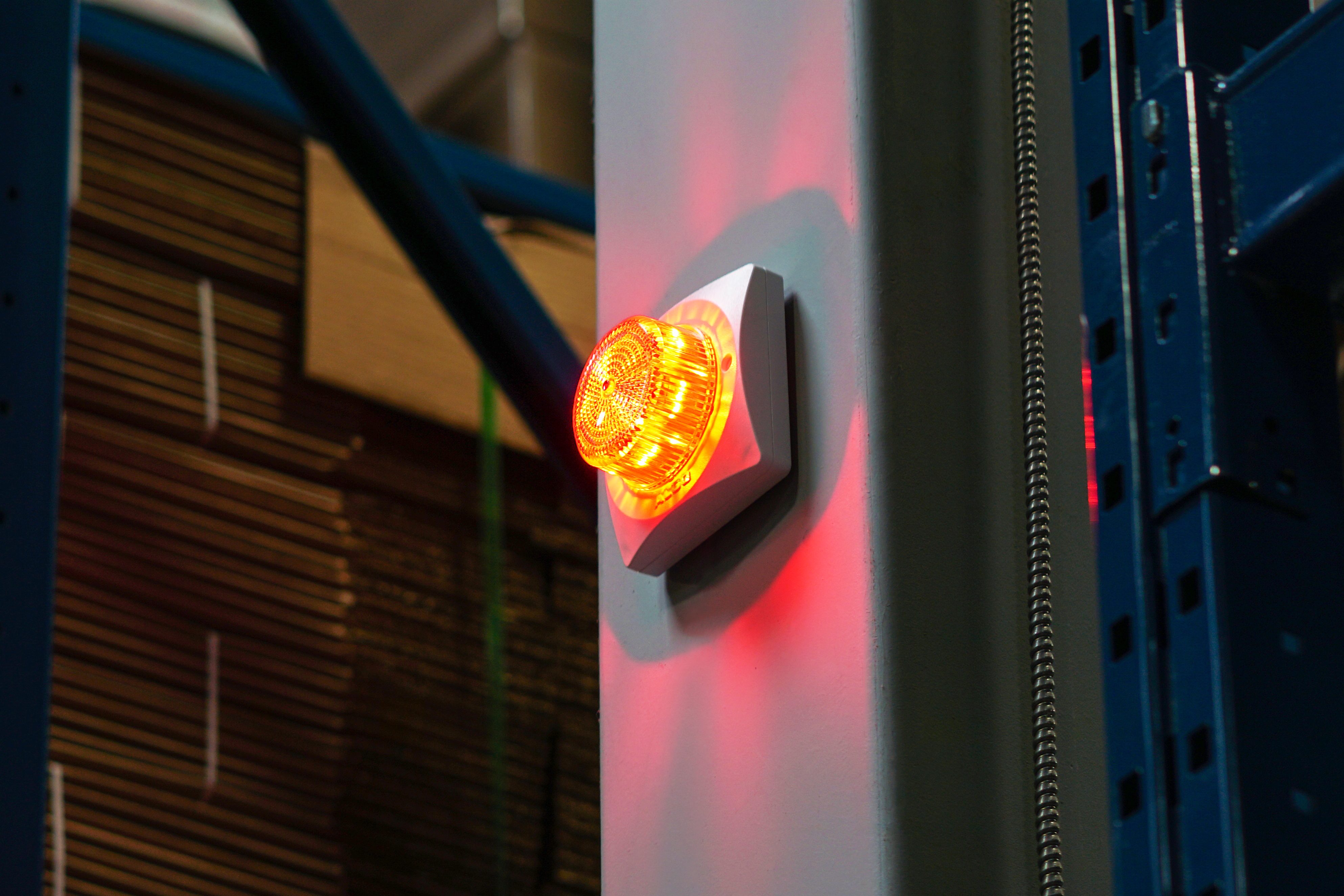 An image of an Algo 8138 visual alerter device securely mounted on a wall. The alerter is a square unit with a bright strobe light that can change colours and patters.